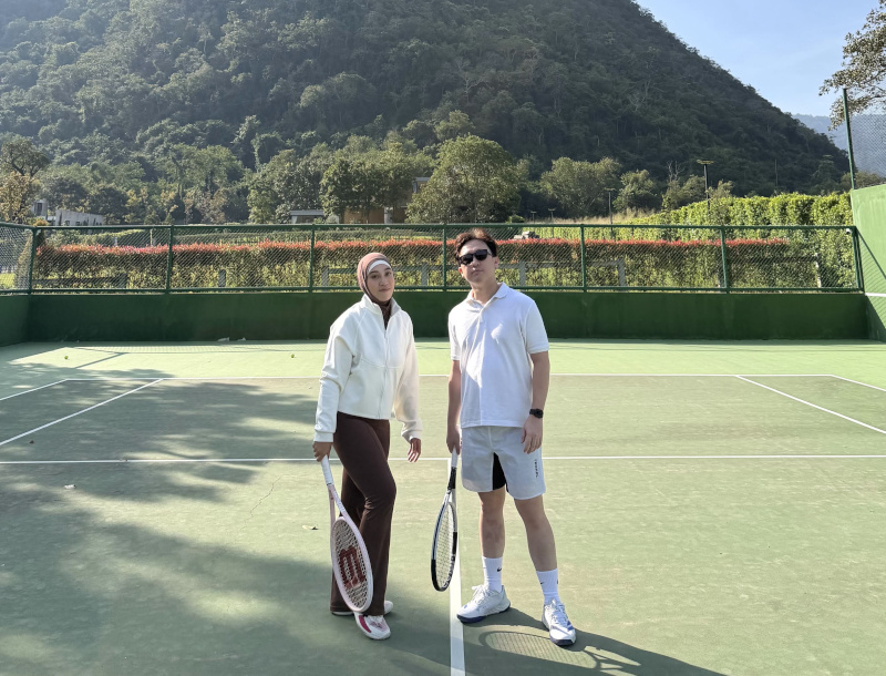 Danu and a friend holding tennis rackets on a court with a mountain backdrop